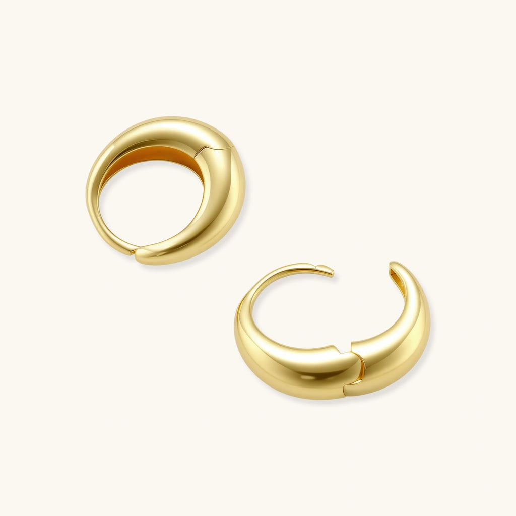 Chunky gold-plated sterling silver huggie hoop earrings with hinged closure mechanism on cream background.